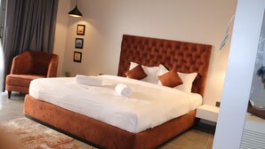 Een hotelkamer met een groot bed, een bruine fauteuil en een wandlamp.