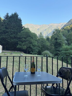 Et bord med en vinflaske og to glas på en balkon med udsigt til et bjerg.