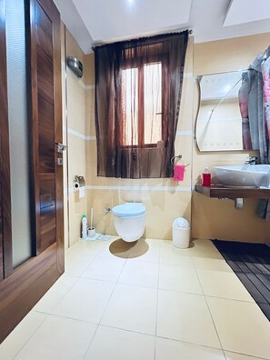 Baño con inodoro, lavamanos, espejo y ventana con cortinas.