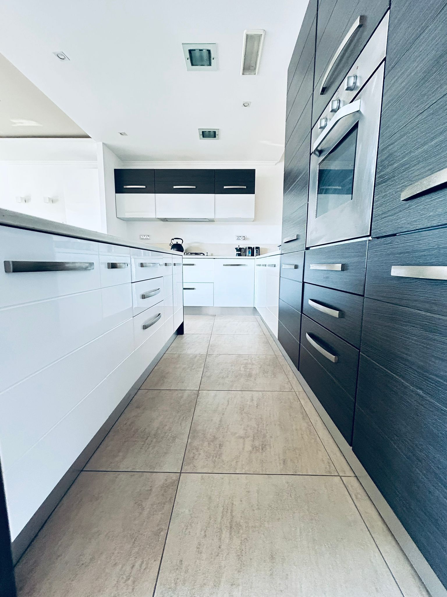 Une cuisine moderne avec des meubles blancs, un mur d’accent en bois foncé et un four encastré.