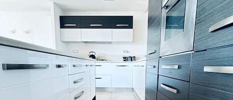 A modern kitchen with white cabinetry, a dark wood accent wall, and a built-in oven.