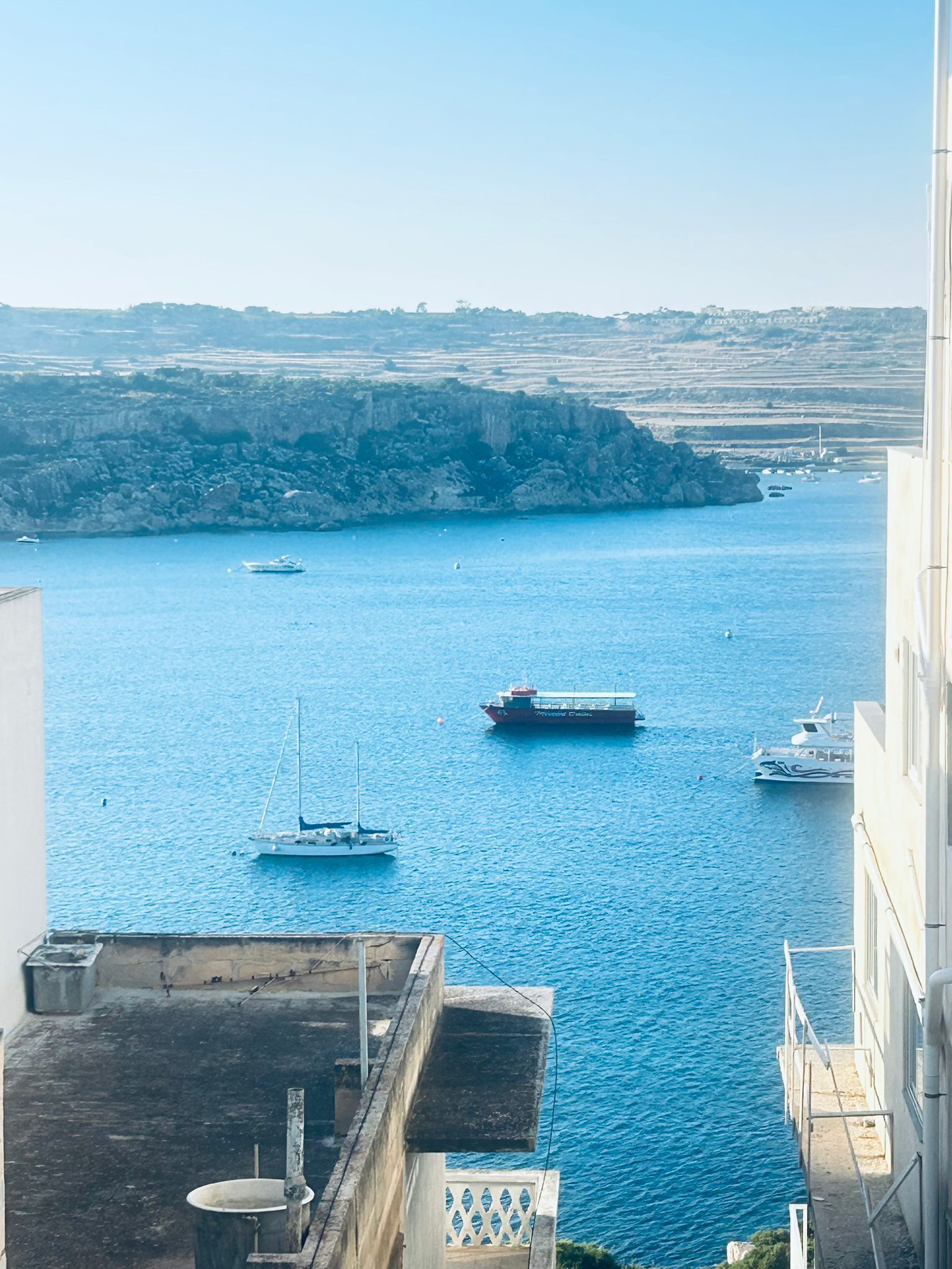 Vista costeira com um porto, barcos e uma linha de costa distante.