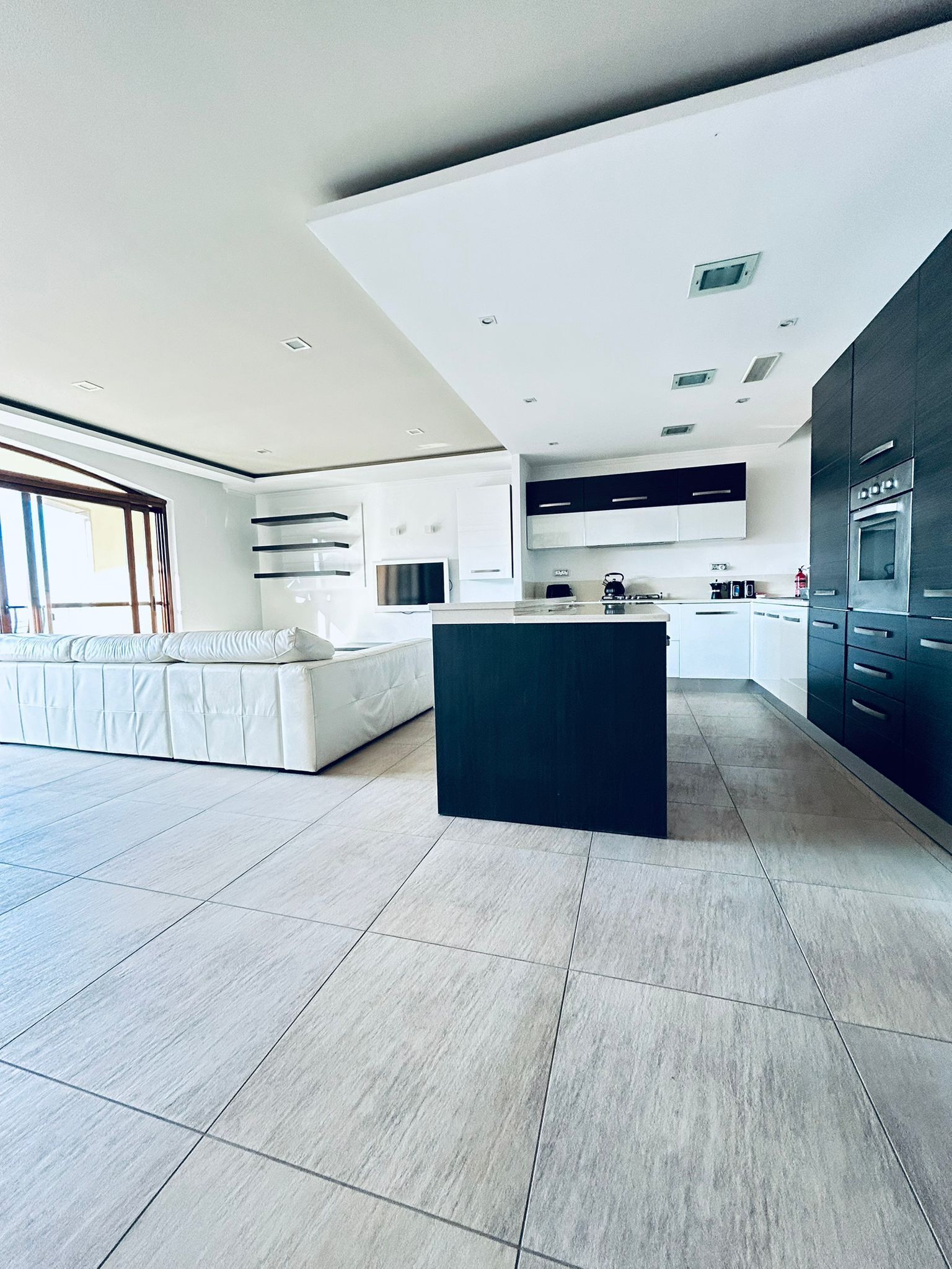 A modern kitchen with a central island, built-in appliances, and a large window.