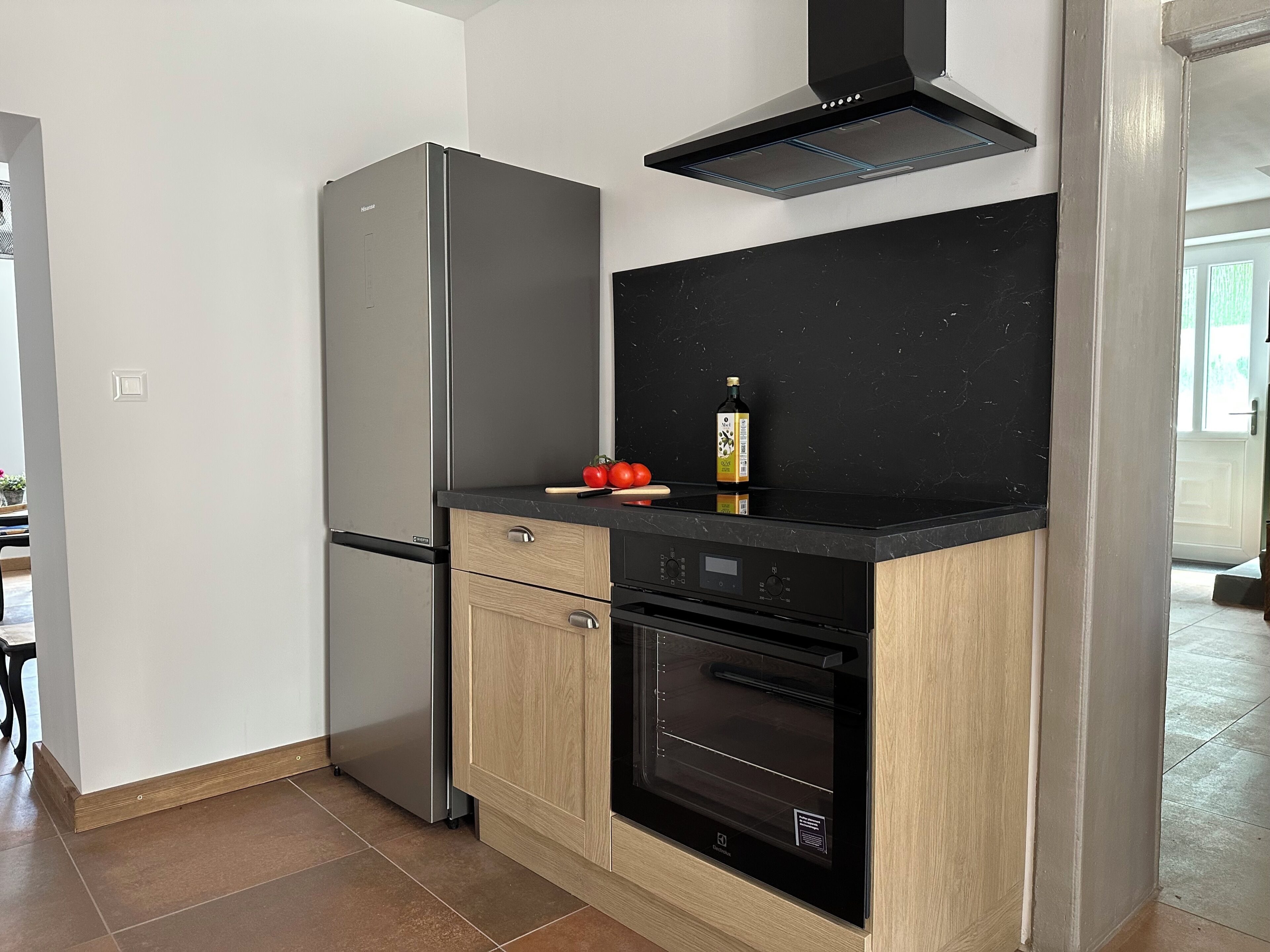 A compact kitchen with a built-in oven, a stainless steel refrigerator, and a black countertop.
