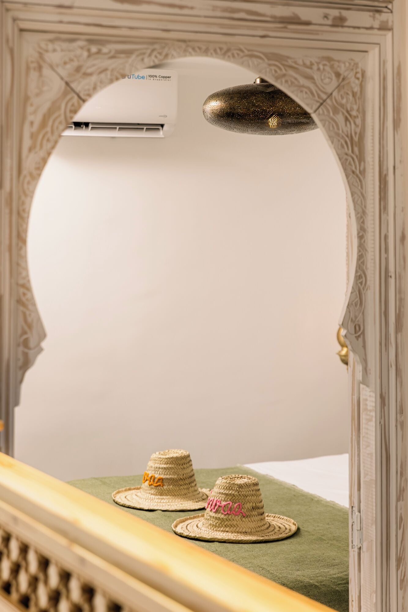 Une pièce avec un miroir décoratif, un appareil de climatisation et deux chapeaux posés sur une surface verte.