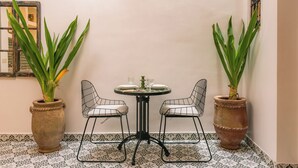 A corner with two metal chairs, a small round table, and two potted plants with long green leaves. - Your Douiria (Marrakech)