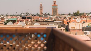 A balcony with a lattice railing overlooking a cityscape with buildings and a prominent tower. - Your Douiria (Marrakech)