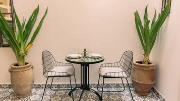 Un coin avec une table ronde dressée pour deux personnes, deux chaises, deux plantes en pot et un sol à motifs.