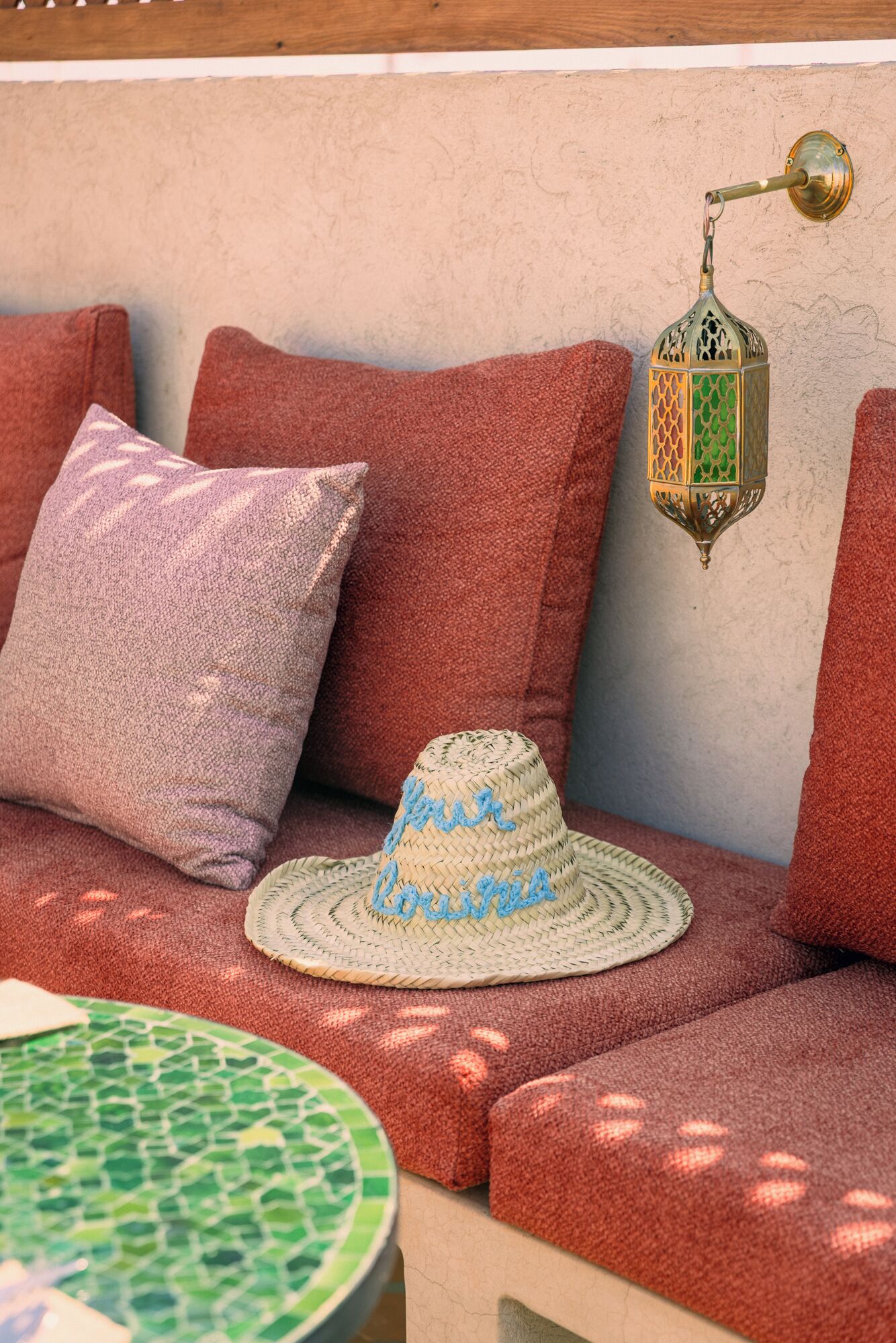 A cozy seating area with a woven hat on a cushion, a lantern, and a round table with a green mosaic top.