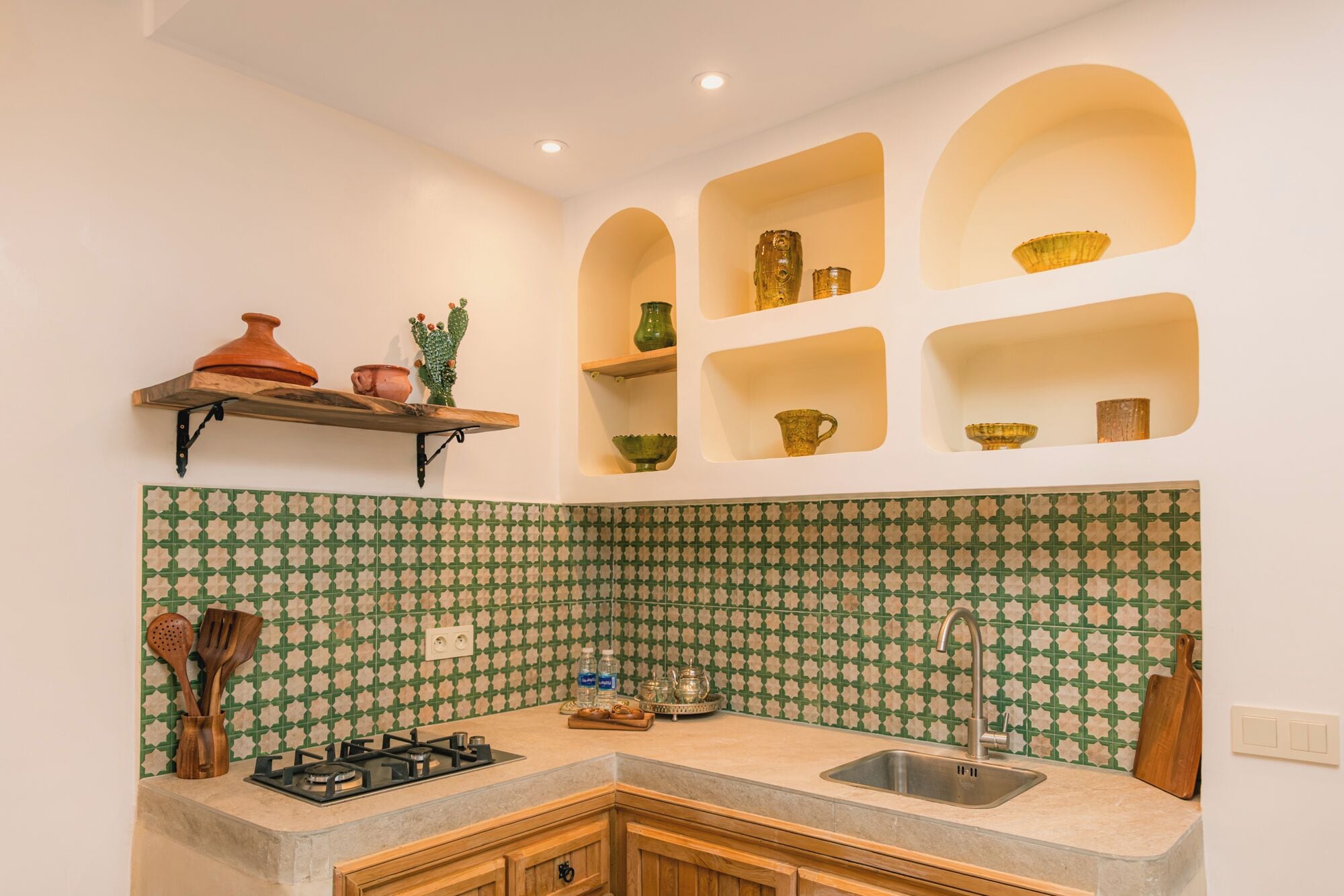 Cozinha com fogão a gás, pia e painel de parede com padrão verde e bege.