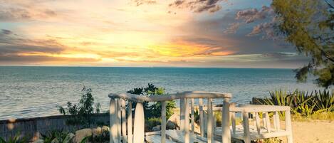 Un banco de madera con vista a una playa y al atardecer sobre el mar.