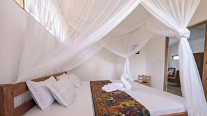 Una stanza con un letto, tende bianche, una testiera in legno e una coperta a motivi.