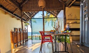 A dining area with a view of the ocean, a thatched roof, and a table with chairs.
