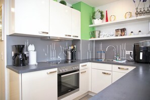 A modern kitchen with white cabinets, a black coffee maker, a sink, and a stove. - "Sandkorn 5" Modern vacation rental with a south-facing balcony, two bedrooms, and proximity to the beach (Grömitz)