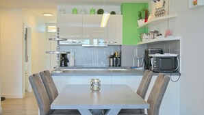 Een moderne keuken met witte kastjes, een grijs aanrechtblad en een eethoek met een tafel en stoelen.