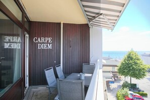 Ein Balkon mit Esstisch und Stühlen, Blick aufs Meer, und ein Schild mit der Aufschrift 'CARPE DIEM'.