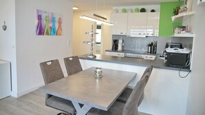 Een moderne keuken met witte kasten, een eettafel met stoelen en een koffieapparaat.