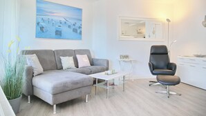Een moderne woonkamer met een grijze bank, een zwarte fauteuil, een kleine witte tafel en een groot schilderij van een strandgezicht.