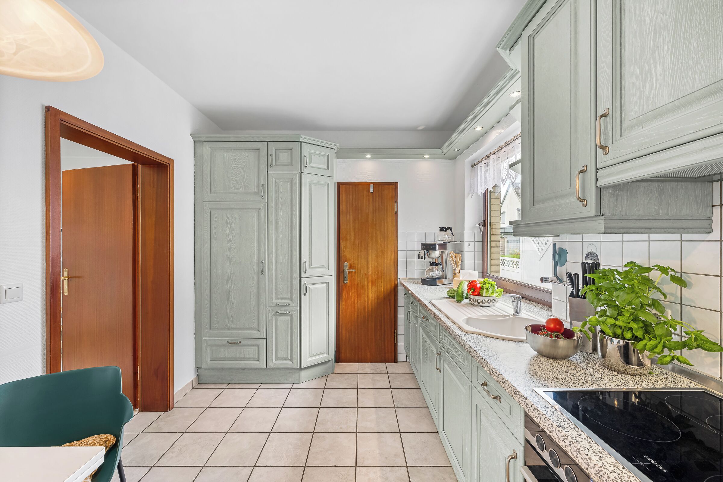 A modern kitchen with light green cabinetry, a black stove, and a countertop with a bowl of vegetables.