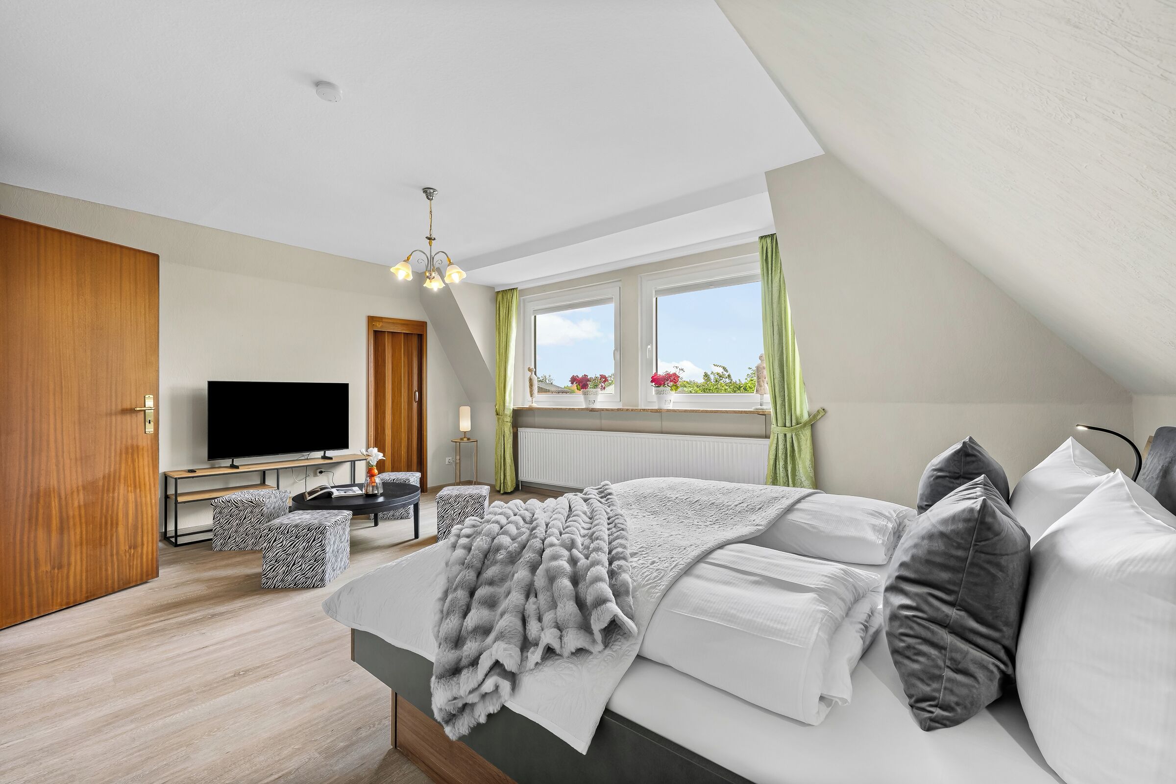 A modern bedroom with a large bed, a television, a desk, and a window with curtains.