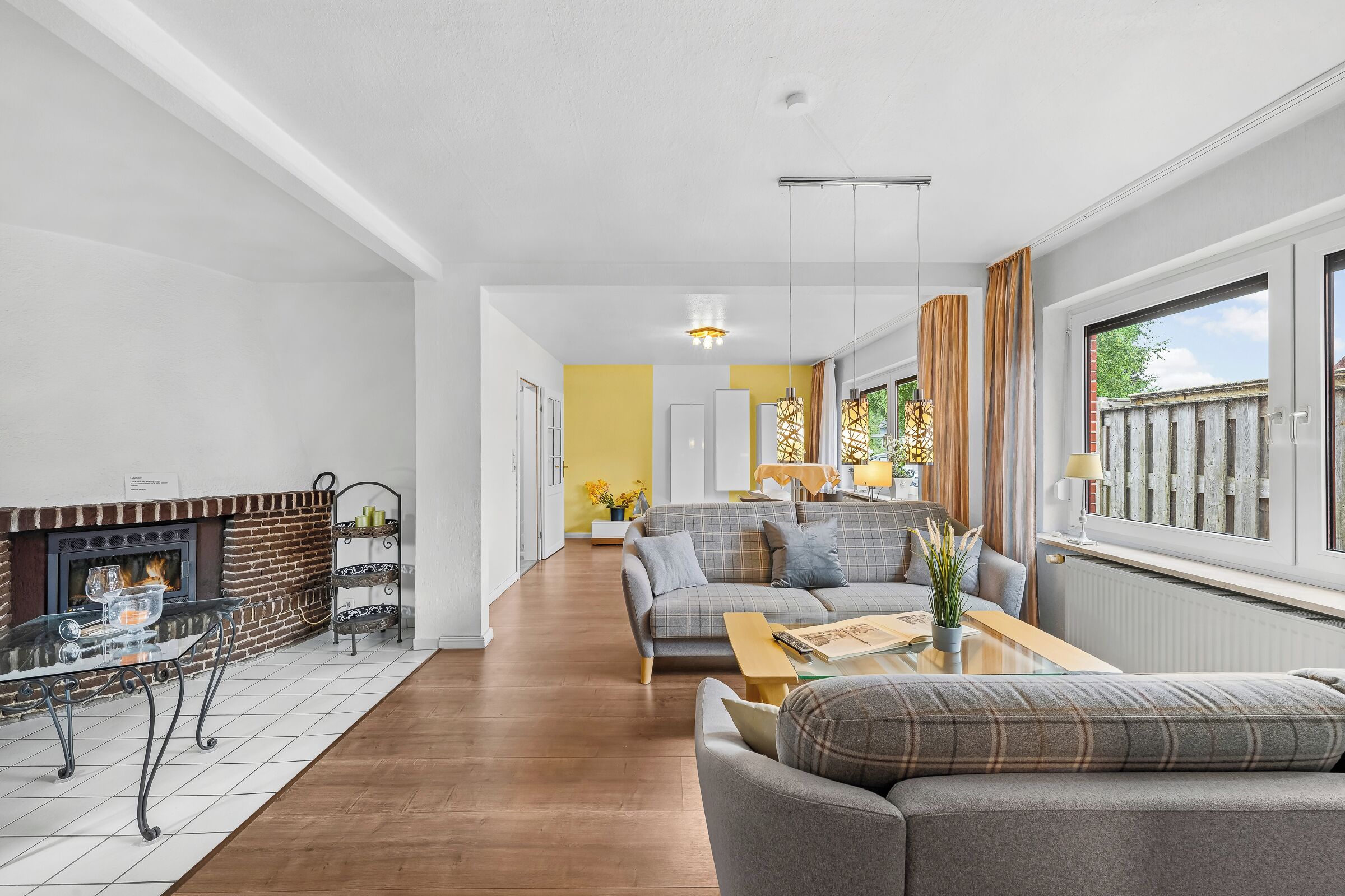 Een moderne woonkamer met een open haard, een zithoek, een salontafel en een eetgedeelte met gele wanden.