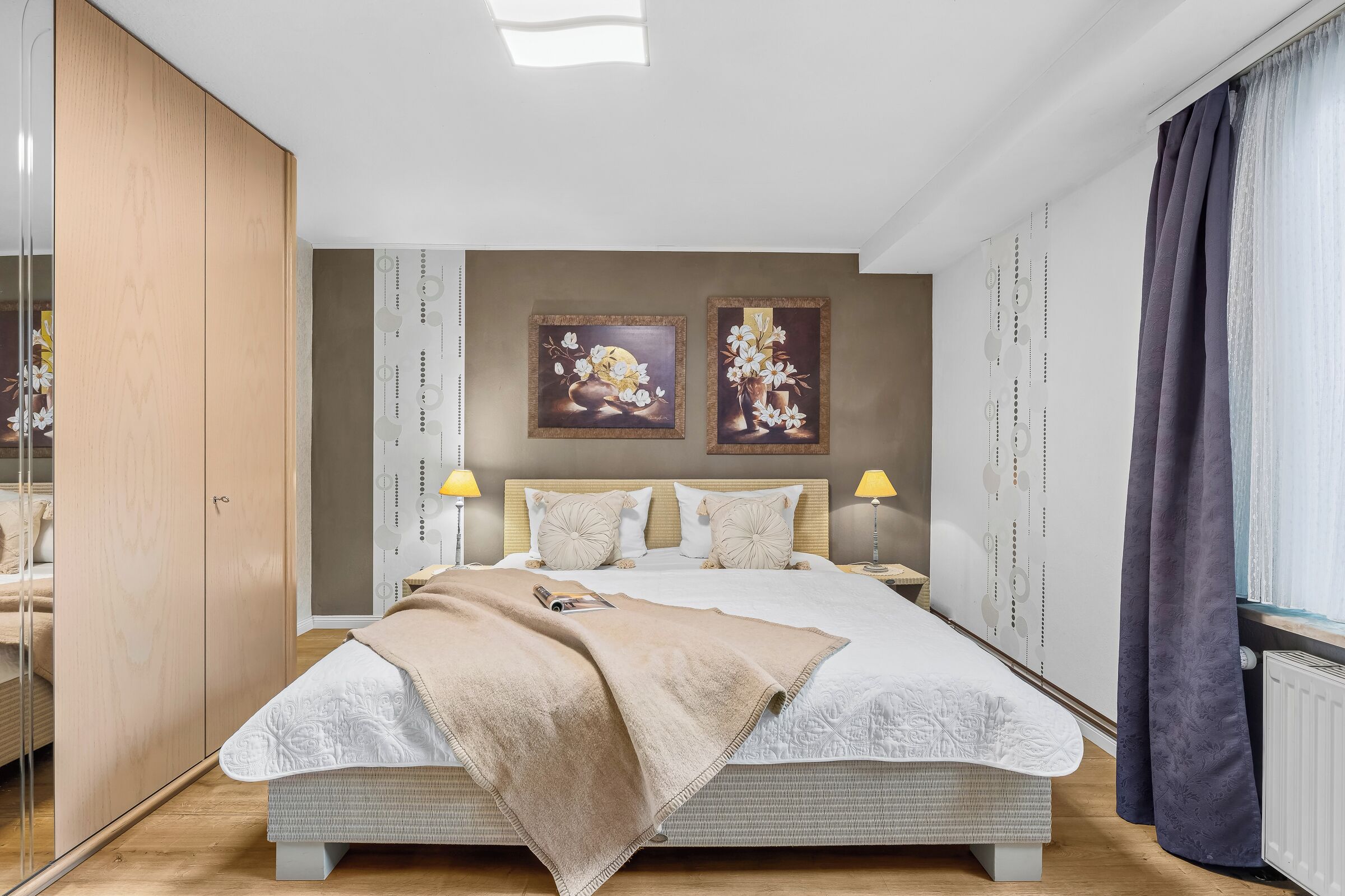 Ein Schlafzimmer mit einem großen Bett, zwei Wandlampen und zwei gerahmten Bildern.