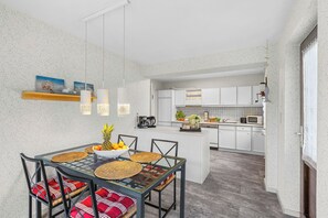 Een moderne keuken met witte kastjes, een eethoek met een glazen tafel, en een hangende lamp.
