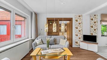Een moderne woonkamer met een bank, een salontafel, een televisie en een raam met uitzicht op een rode gevel.