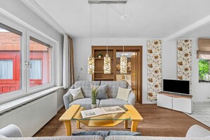 Een moderne woonkamer met een bank, een salontafel, een televisie en een raam met uitzicht op een rode gevel.