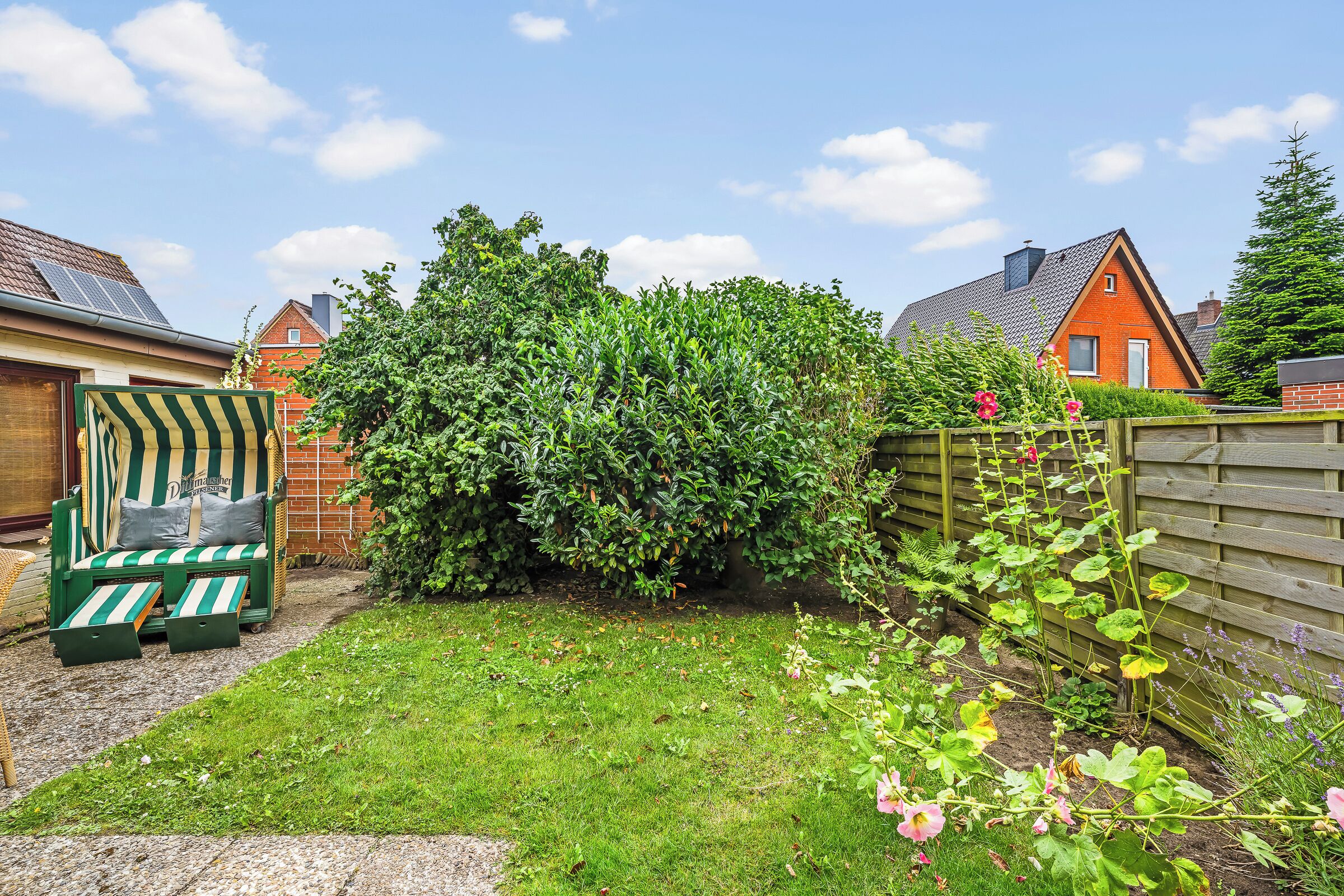 Een tuin met gazon, houten omheining en een groene zitplek.