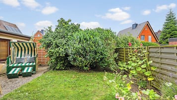 Een tuin met gazon, houten omheining en een groene zitplek.
