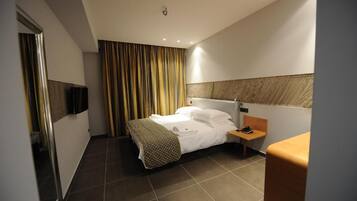 Una habitación de hotel con cama, mesita de noche y televisor montado en la pared.