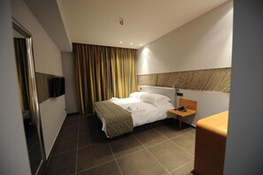 A hotel room with a bed, bedside table, and a TV mounted on the wall.