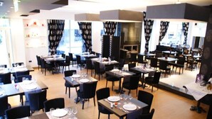 A restaurant with multiple tables and chairs, some with plates and glasses set. - Hotel ILIANA (Filippiada)