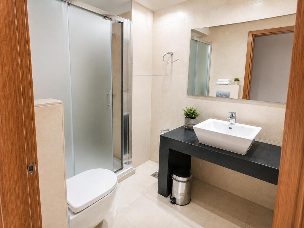 Une salle de bain moderne avec une douche à l’italienne en verre, des toilettes blanches, un plan de toilette noir avec un lavabo et un miroir au-dessus du lavabo.