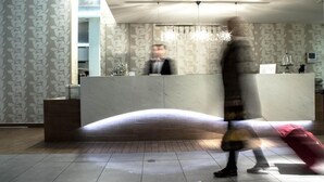 A hotel reception area with a curved reception desk, patterned wallpaper, and a chandelier. - Hotel ILIANA (Filippiada)