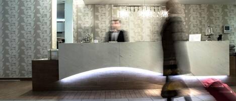 A hotel reception area with a curved reception desk, patterned wallpaper, and a chandelier.