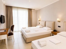 Una habitación de hotel con tres camas, un escritorio, una silla, un televisor y una lámpara.