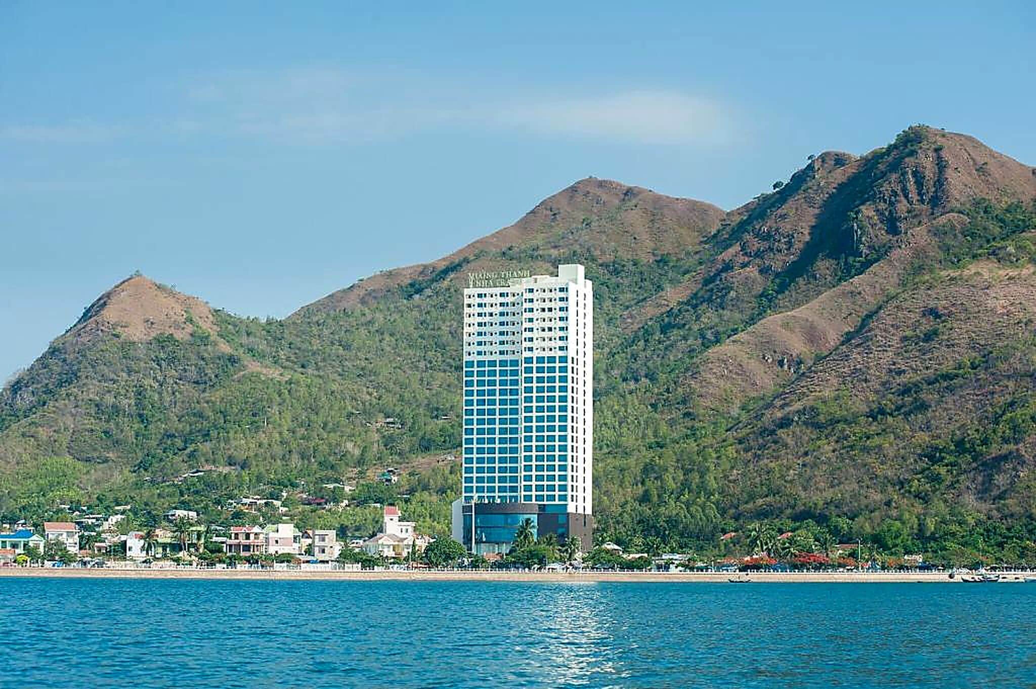 Un hotel moderno de gran altura con fachada de vidrio, ubicado frente al agua y montañas al fondo.