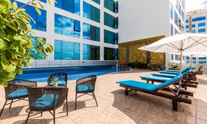 Ein Poolbereich mit Liegestühlen, einem Tisch und Blick auf ein Gebäude mit großen Fenstern.