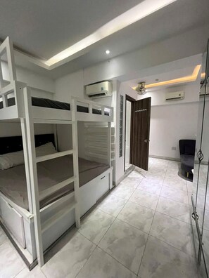 Ein Zimmer mit Etagenbetten, einer Klimaanlage, einer Tür und einem Fliesenboden.