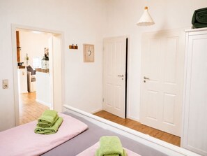 Ein Hotelzimmer mit Bett, Spiegel, Tür und einem Flur, der zu einem weiteren Zimmer führt.