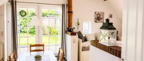 A dining area with a wooden table and chairs, a window with curtains, and a view of greenery outside.