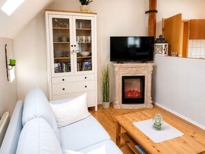 Ein Wohnzimmer mit einer Couch, einem Fernseher, einer Vitrine und einem Kamin.