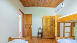 A room with two wooden bunk beds, a wooden wardrobe, a chair, and a door leading to another room.
