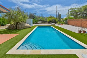 Ein rechteckiger Pool mit klarer, blauer Wasseroberfläche, umgeben von einem gepflegten Rasen und verschiedenen Wüstenpflanzen.