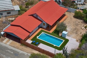 Ein zweistöckiges Haus mit rotem Dach, Schwimmbad und umzäunter Garten.