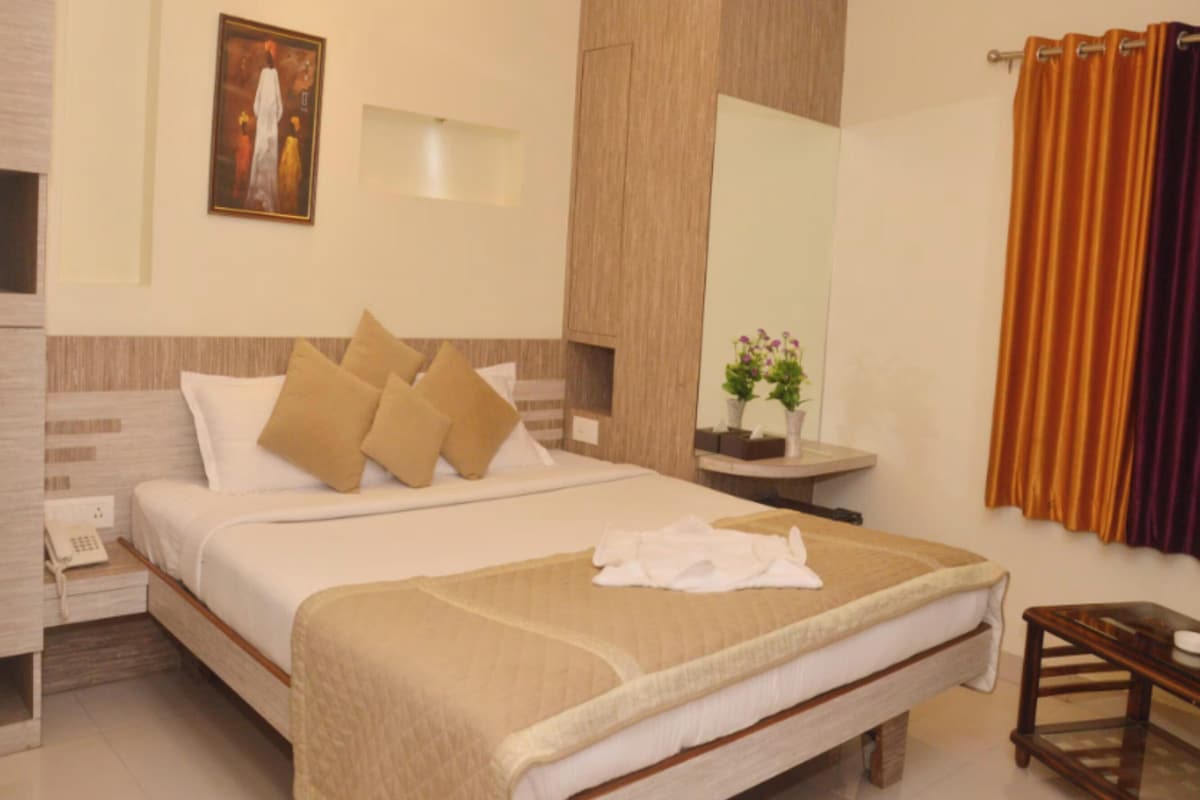 A hotel room with a bed, bedside table, a mirror, a painting, and a window with curtains.