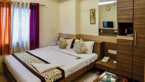 A hotel room with a bed, bedside table, and a mirror. - Muzzafarpur Inn Shivam on Motijheel Rd. (Muzaffarpur)