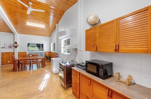 Una cocina con gabinetes de madera, un microondas, una estufa y un comedor con sillas y una mesa.